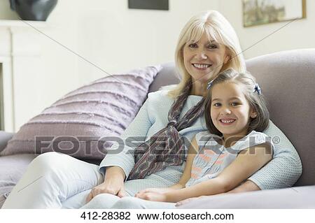 Stock Image - Portrait smiling grandmother and granddaughter on living room sofa. Fotosearch
