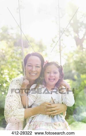 Stock Image - Portrait smiling mother hugging daughter on swing in park. Fotosearch