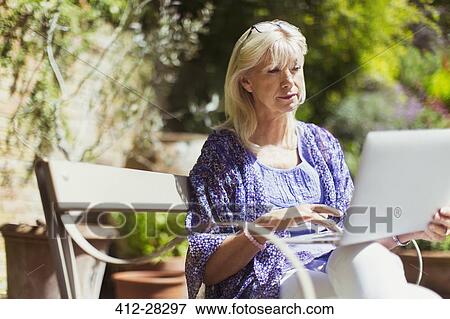 Senior woman using laptop on sunny garden bench View Large Photo Image Stock Photo - Senior woman using laptop on sunny garden bench. Fotosearch