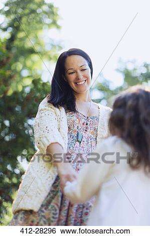 Stock Photograph - Smiling mother and daughter holding hands outdoors. Fotosearch