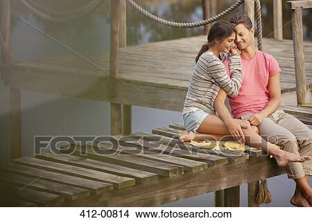 Picture - Affectionate couple sitting on dock over lake. Fotosearch