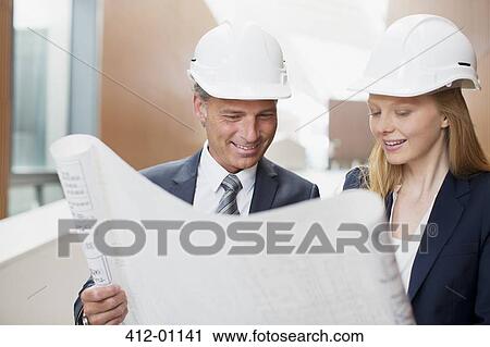Stock Image - Architects wearing hard-hats and reviewing blueprints. Fotosearch