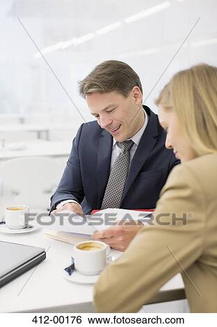 Stock Photograph - Businessman and businesswoman reviewing paperwork at restaurant. Fotosearch