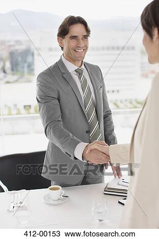 Stock Image - Businessman and businesswoman shaking hands at restaurant table. Fotosearch