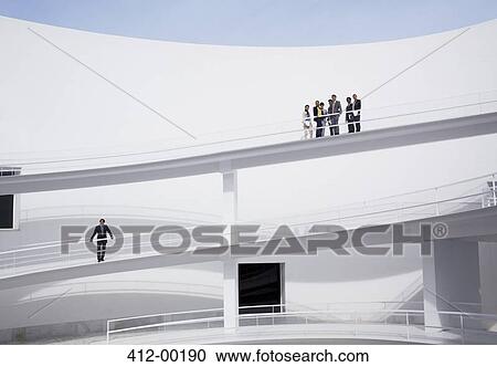 Stock Image - Businessman below business people on elevated walkway. Fotosearch