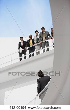 Picture - Businessman looking up at business people on elevated walkway. Fotosearch