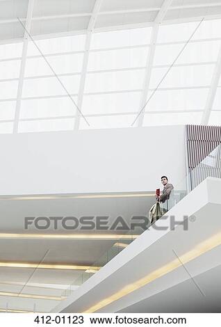 Stock Image - Businessman standing at glass balcony railing in modern building. Fotosearch