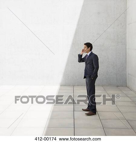 Businessman standing in shade and talking on cell phone View Large Photo Image Picture - Businessman standing in shade and talking on cell phone. Fotosearch