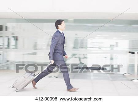 Businessman with suitcase rushing along airport corridor View Large Photo Image Stock Photo - Businessman with suitcase rushing along airport corridor. Fotosearch