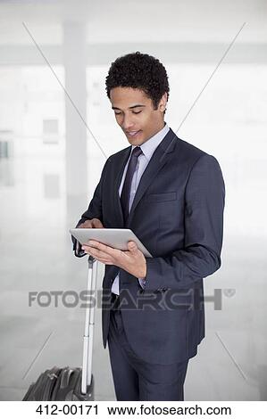 Businessman with suitcase using digital tablet in airport View Large Photo Image Stock Image - Businessman with suitcase using digital tablet in airport. Fotosearch