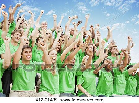Stock Photo - Crowd in green t-shirts cheering with arms raised. Fotosearch