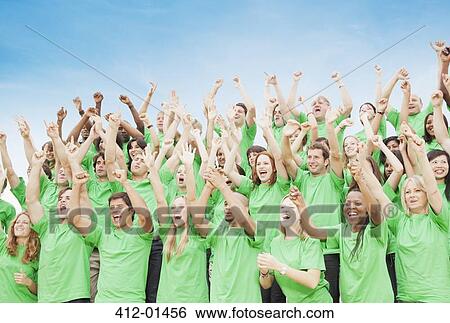 Crowd in green t-shirts cheering with arms raised View Large Photo Image Stock Photograph - Crowd in green t-shirts cheering with arms raised. Fotosearch