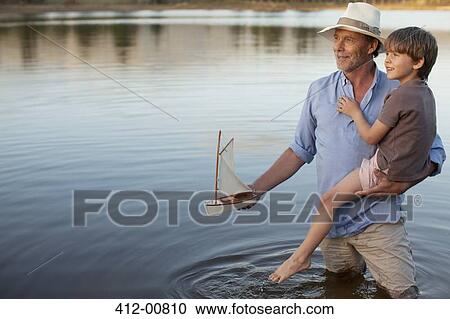 Grandfather and grandson with toy sailboat in lake View Large Photo Image Stock Image - Grandfather and grandson with toy sailboat in lake. Fotosearch