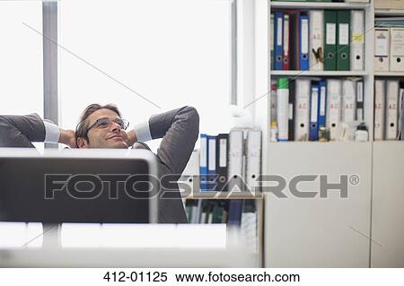 Happy businessman with head back and hands behind head in office View Large Photo Image Stock Photography - Happy businessman with head back and hands behind head in office. Fotosearch