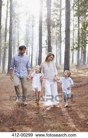 Stock Photo - Happy family holding hands and walking in sunny woods. Fotosearch