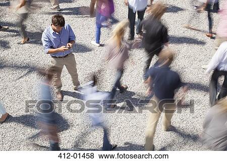 Man checking cell phone among rushing crowd View Large Photo Image Stock Photo - Man checking cell phone among rushing crowd. Fotosearch