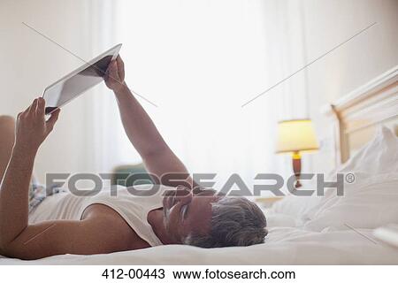 Man laying in bed and using digital tablet View Large Photo Image Stock Image - Man laying in bed and using digital tablet. Fotosearch