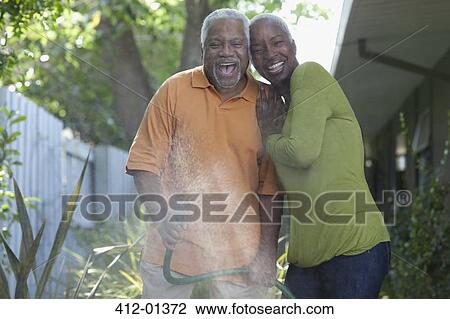 Stock Image - Older couple watering plants in backyard. Fotosearch