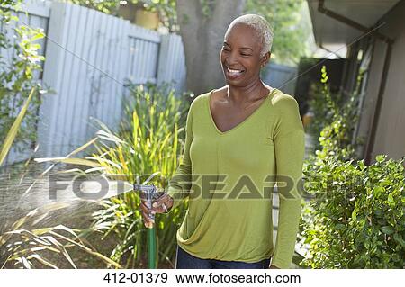 Older woman watering plants on beach View Large Photo Image Stock Photo - Older woman watering plants on beach. Fotosearch