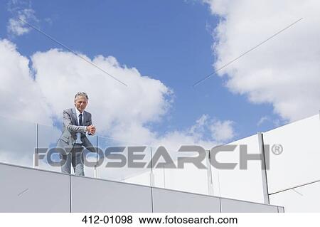 Stock Photo - Portrait of confident businessman with hands clasped on balcony. Fotosearch