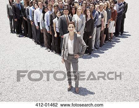 Stock Image - Portrait of confident businesswoman with team of business people in background. Fotosearch