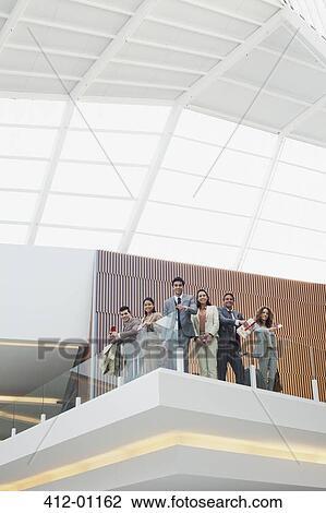 Portrait of smiling business people at glass railing of balcony in modern office View Large Photo Image Stock Image - Portrait of smiling business people at glass railing of balcony in modern office. Fotosearch