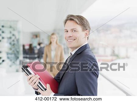 Portrait of smiling businessman holding paperwork in corridor View Large Photo Image Stock Image - Portrait of smiling businessman holding paperwork in corridor. Fotosearch