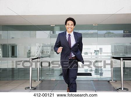 Stock Image - Portrait of smiling businessman running in front of airport. Fotosearch