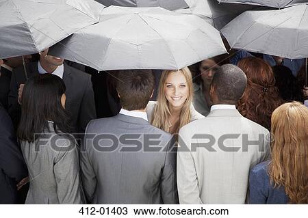 Stock Image - Portrait of smiling businesswoman surrounded by crowd with umbrellas. Fotosearch