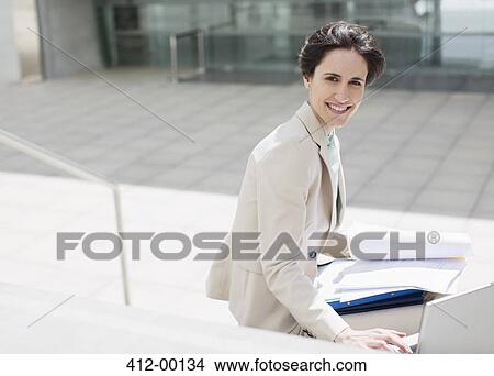 Portrait of smiling businesswoman with laptop and paperwork outside building View Large Photo Image Picture - Portrait of smiling businesswoman with laptop and paperwork outside building. Fotosearch