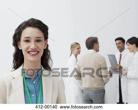 Stock Image - Portrait of smiling businesswoman with doctors in background. Fotosearch