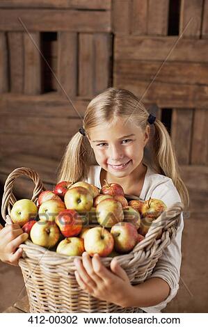 Stock Image - Portrait of smiling girl holding bushel of apples. Fotosearch