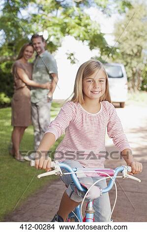 Portrait of smiling girl on bicycle with parents in background View Large Photo Image Picture - Portrait of smiling girl on bicycle with parents in background. Fotosearch