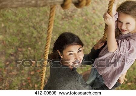 Stock Photo - Portrait of smiling mother and daughter on swing. Fotosearch