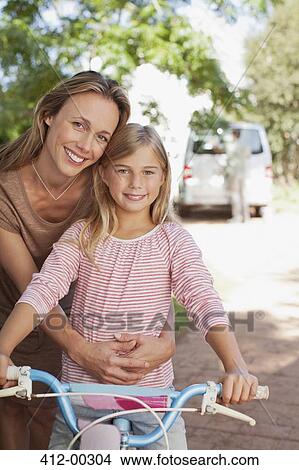 Portrait of smiling mother hugging daughter on bicycle View Large Photo Image Picture - Portrait of smiling mother hugging daughter on bicycle. Fotosearch