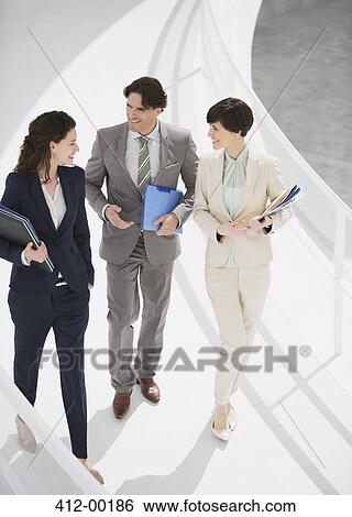 Smiling business people talking and walking down elevated walkway View Large Photo Image Stock Photograph - Smiling business people talking and walking down elevated walkway. Fotosearch