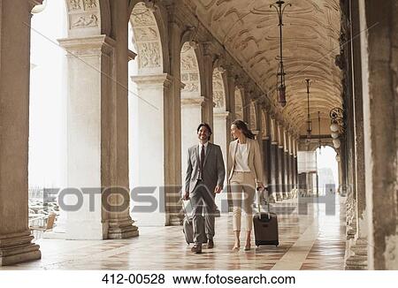 Smiling businessman and businesswoman pulling suitcases along corridor in Venice View Large Photo Image Stock Photo - Smiling businessman and businesswoman pulling suitcases along corridor in Venice. Fotosearch