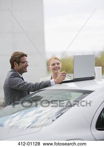 Smiling businessman and businesswoman using laptop on top of car View Large Photo Image Stock Photo - Smiling businessman and businesswoman using laptop on top of car. Fotosearch
