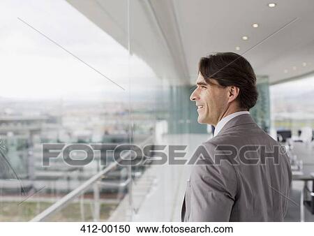Stock Image - Smiling businessman looking out window of conference room. Fotosearch
