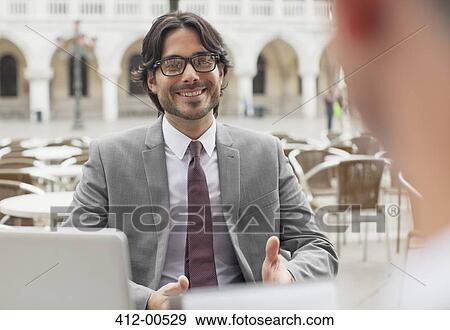 Stock Photo - Smiling businessman talking to co-worker at sidewalk cafe. Fotosearch