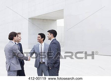 Stock Photo - Smiling businessmen shaking hands outside cultural center. Fotosearch