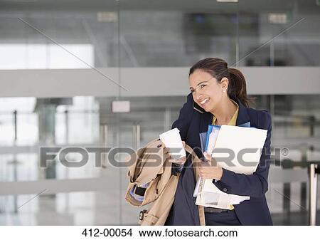 Picture - Smiling businesswoman multitasking on cell phone with coffee and paperwork. Fotosearch