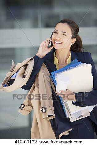 Smiling businesswoman talking on cell phone and carrying paperwork View Large Photo Image Stock Image - Smiling businesswoman talking on cell phone and carrying paperwork. Fotosearch