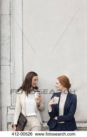 Smiling businesswomen drinking coffee and talking against building wall View Large Photo Image Stock Photograph - Smiling businesswomen drinking coffee and talking against building wall. Fotosearch