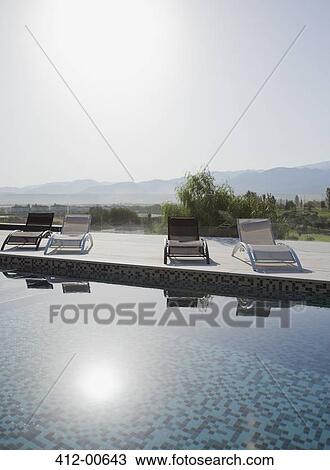 Stock Image - Sun shining over lounge chairs and swimming pool. Fotosearch