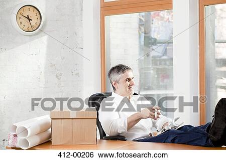 Businessman relaxing at desk in office View Large Photo Image Stock Photograph - Businessman relaxing at desk in office. Fotosearch