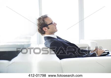 Businessman sitting on sofa in office lobby View Large Photo Image Stock Photo - Businessman sitting on sofa in office lobby. Fotosearch
