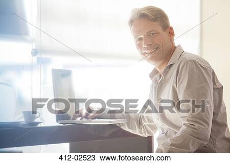 Stock Image - Businessman smiling at laptop. Fotosearch