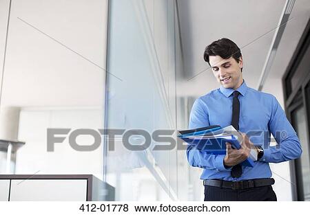 Stock Photo - Businessman using digital tablet in office hallway. Fotosearch