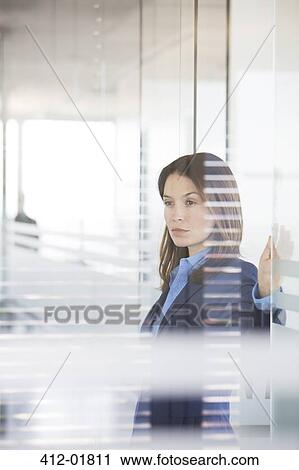 Stock Image - Businesswoman standing in office hallway. Fotosearch